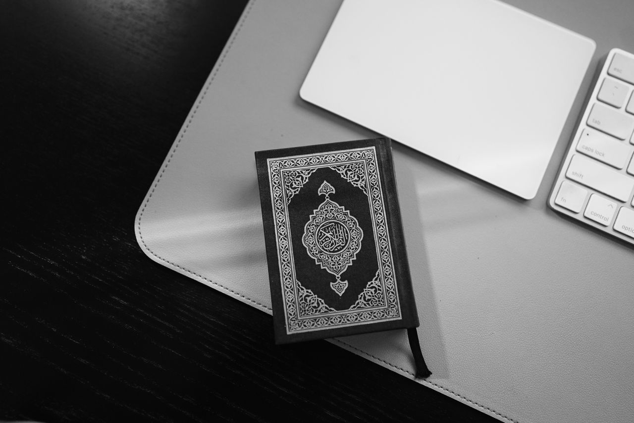 Black and white image of a Quran near a computer keyboard, signifying the blend of tradition and technology.
